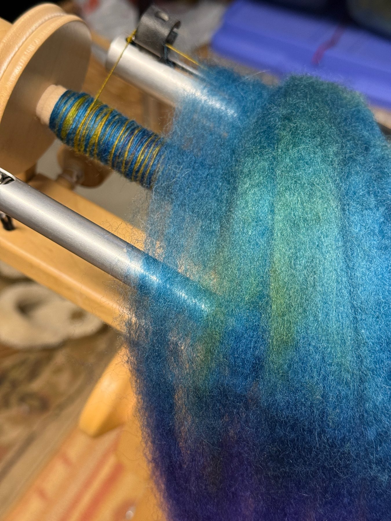 Hand-dyed teal Targhee wool roving feeding onto a spinning wheel bobbin